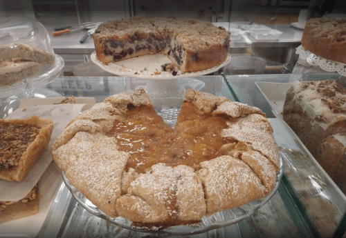 A display case filled with various baked goods, including fruit-filled pies and crumb-topped cakes.