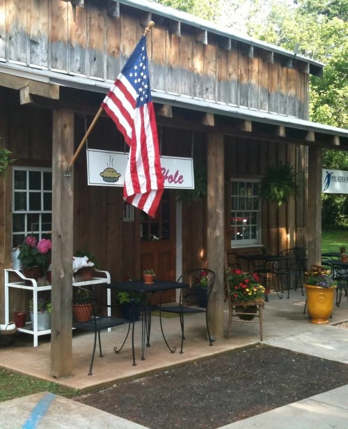 A rustic building with a wooden facade, featuring a U.S. flag, outdoor seating, and potted plants.