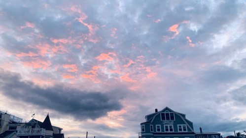 A colorful sunset sky with pink and gray clouds above a green house.