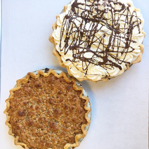 Two pies on a white background: one with a golden crust and a nutty filling, the other topped with whipped cream and chocolate drizzle.