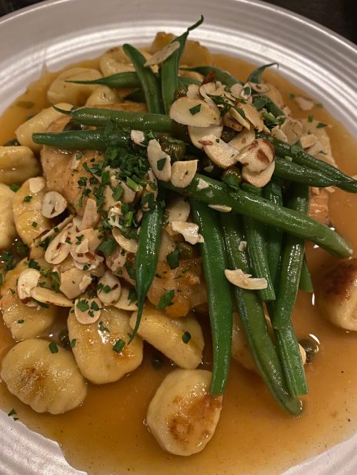 A plate of gnocchi topped with green beans, sliced almonds, and a savory sauce.