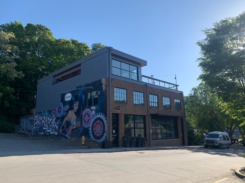 A modern building with a colorful mural on the side, surrounded by trees and parked cars.