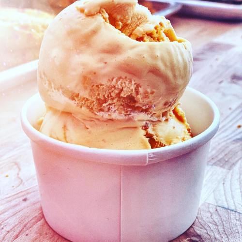A close-up of a cup filled with two scoops of creamy orange ice cream on a wooden surface.