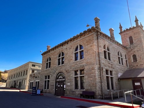 Historic stone building with arched windows, labeled "Penitentiary," under a clear blue sky.