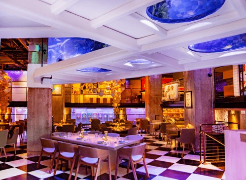 A modern restaurant interior with checkered floors, stylish seating, and colorful lighting.