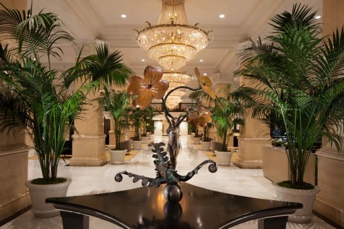 Luxurious hotel lobby featuring a grand chandelier, elegant floral sculptures, and lush greenery.