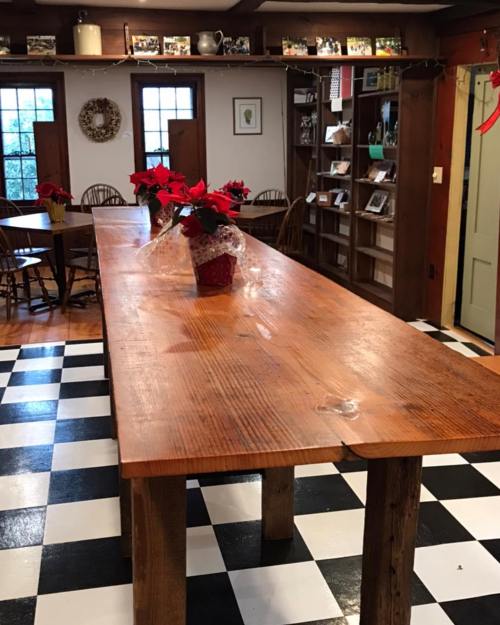 A rustic dining area with a large wooden table, red poinsettias, and a black-and-white checkered floor.