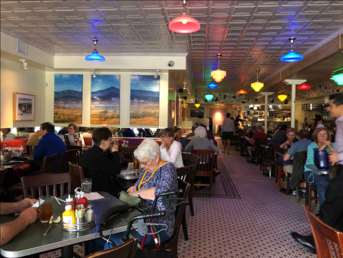 A bustling restaurant interior with colorful pendant lights, diners at tables, and a warm, inviting atmosphere.