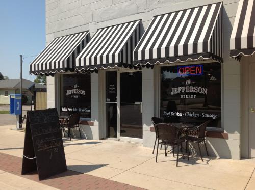 Exterior of Jefferson Street restaurant with striped awnings, open sign, and outdoor seating area. Menu board visible.