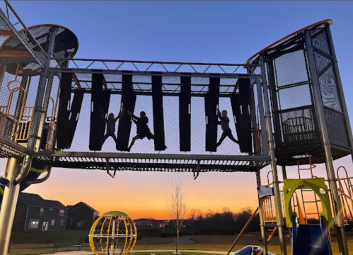 Children playing on a playground structure at sunset, with silhouettes against a colorful sky.