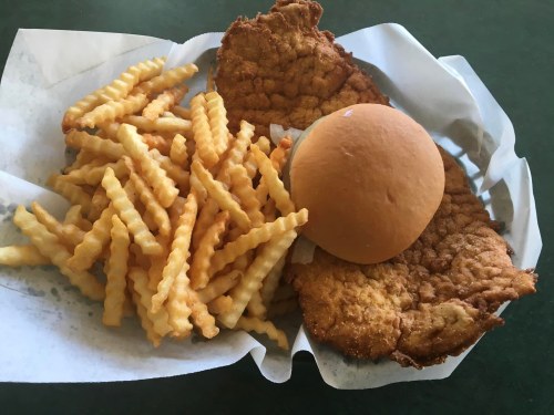A plate with two fried chicken cutlets, a soft bun, and a serving of crinkle-cut fries on a paper-lined tray.