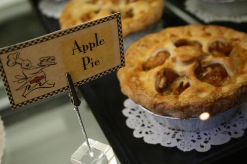 A freshly baked apple pie displayed in a glass case with a sign indicating its name.