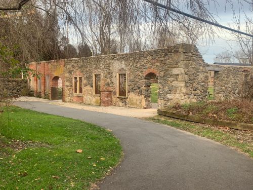 Ruins of a stone building with arched windows, surrounded by grass and a pathway. Trees in the background.