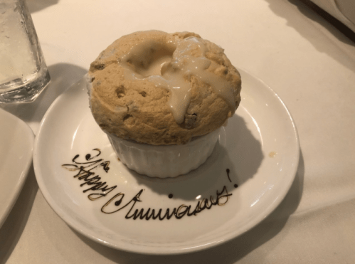 A dessert soufflé with a creamy topping, served in a ramekin on a plate that reads "Happy Anniversary!"