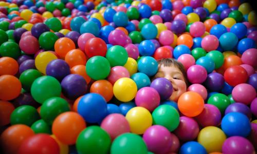 A child peeks out from a colorful ball pit filled with vibrant plastic balls in various colors.