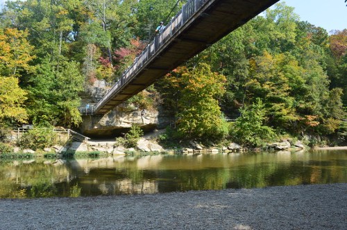 A wooden bridge spans over a river, surrounded by colorful autumn trees and rocky banks.