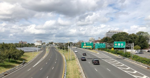 A view of a highway with cars, green directional signs, and a cloudy sky in the background.