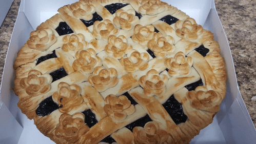 A beautifully crafted pie with a lattice crust and decorative flower-shaped pastry on top, filled with dark fruit filling.