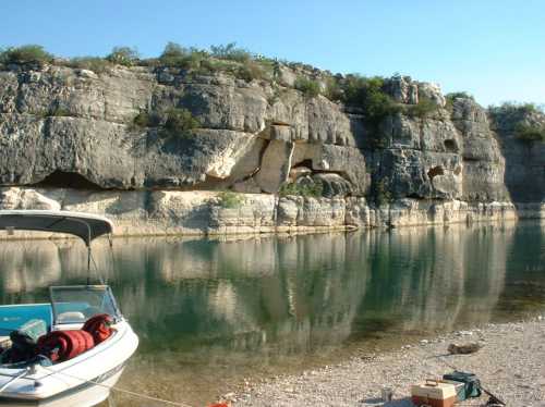 A calm lake with a boat docked on the shore, surrounded by rocky cliffs and clear blue skies.