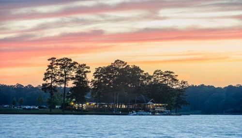 A serene lake at sunset, with a silhouette of trees and a building reflecting warm colors in the sky.