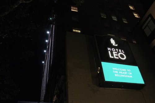 Sign for Hotel Leo at night, featuring the text "Welcome to the Heart of Bellingham" illuminated in blue and white.