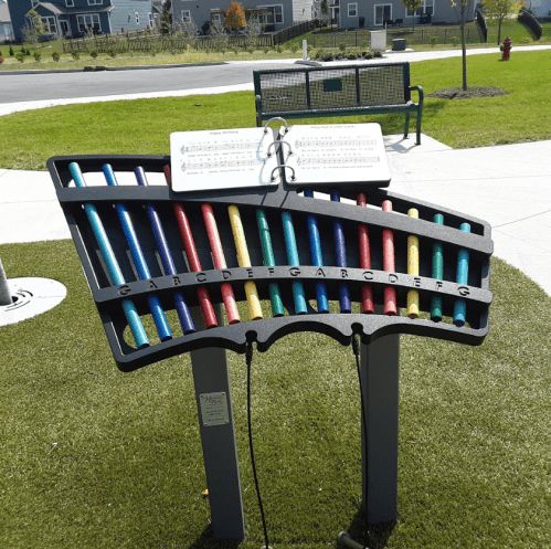 Colorful outdoor musical instrument with notes, featuring bars labeled G to G, set in a grassy park area.