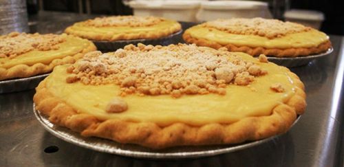 Four pies with a creamy filling and crumb topping, resting on a metal surface.