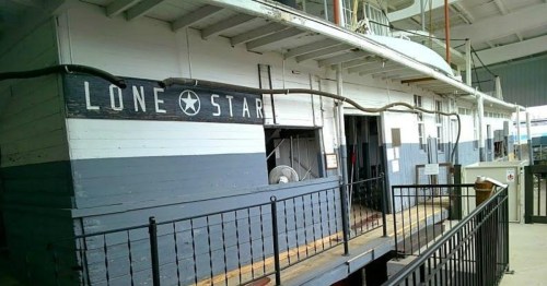 Historic boat named "Lone Star" with a wooden exterior and a railing, docked in a covered area.
