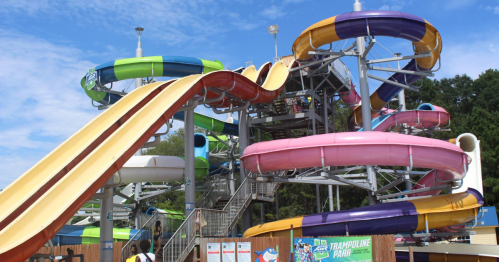 Colorful water slides twist and turn at a water park under a blue sky with fluffy clouds.