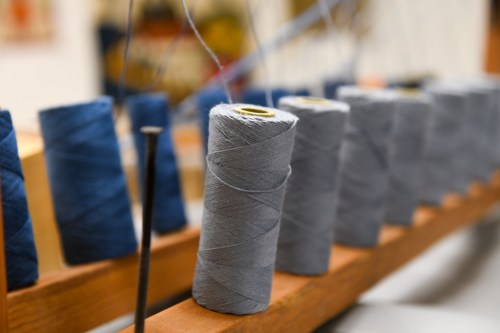 Close-up of spools of thread in various shades of blue and gray, arranged on a wooden rack.