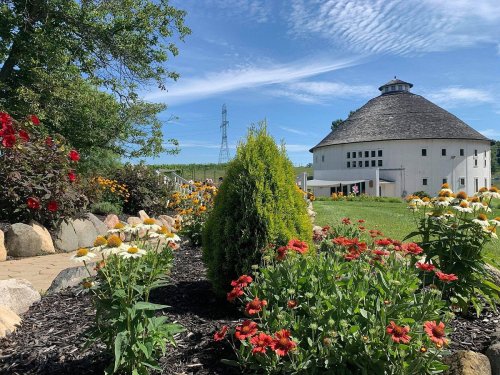 A vibrant garden with colorful flowers in front of a round white building under a blue sky with wispy clouds.