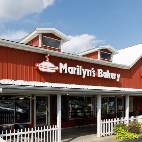 Exterior of Marilyn's Bakery, featuring a red building with a white picket fence and a sign with a pie icon.