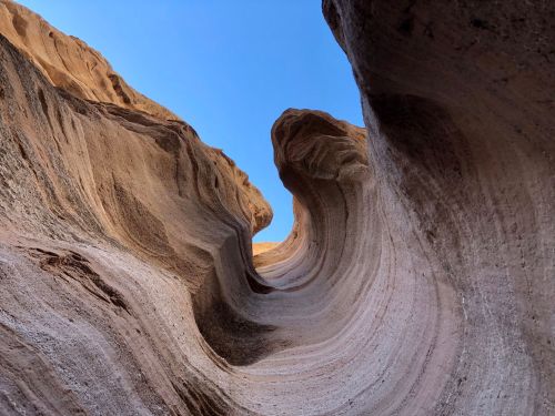 A view looking up at a winding, textured rock formation against a clear blue sky.