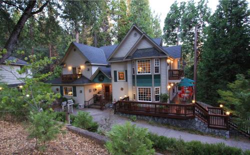 A large, multi-story house surrounded by trees, featuring balconies and a patio with outdoor seating.