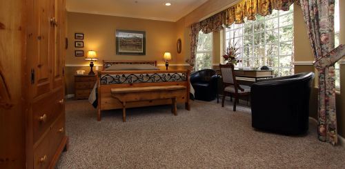 Cozy bedroom with a wooden bed, dresser, and desk, featuring large windows and floral curtains.
