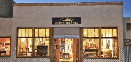 Exterior of a store named "Mediterrània," featuring large windows showcasing decorative items and a warm, inviting atmosphere.