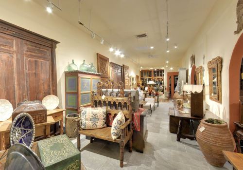 A cozy antique shop filled with various vintage furniture, decor, and artifacts arranged along a well-lit aisle.
