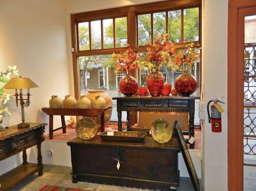 A cozy interior featuring decorative vases, wooden furniture, and autumn-themed arrangements by a window.