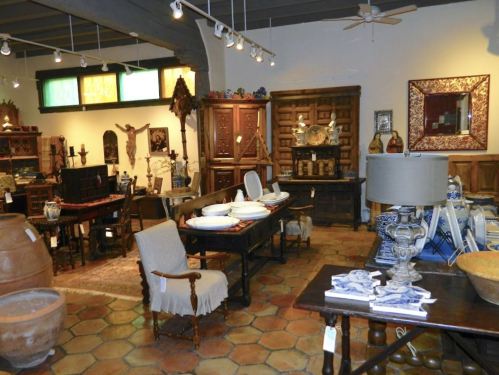 A cozy interior of an antique shop featuring wooden furniture, pottery, and decorative items in warm tones.