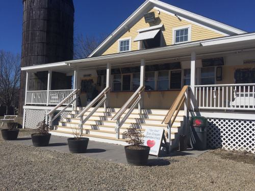 A yellow building with a porch and stairs, featuring a sign for ice cream sandwiches, surrounded by planters.