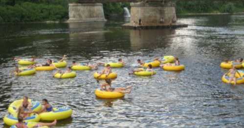 People floating on colorful inner tubes in a river, with a bridge and greenery in the background.