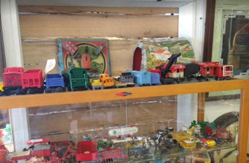 A display of colorful toy trains and vehicles on a shelf, with vintage toys visible in a glass case below.