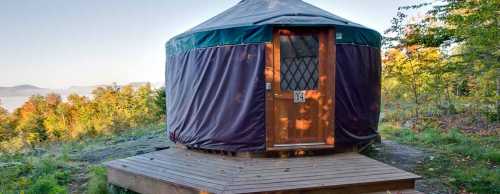 A cozy yurt on a wooden platform, surrounded by trees and a scenic landscape.