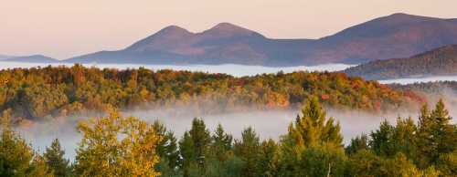 A serene landscape featuring rolling mountains, colorful autumn trees, and a misty valley at sunrise.