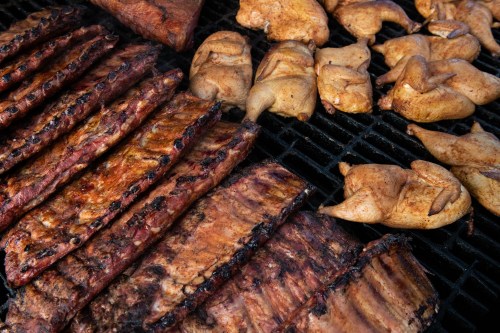Grilled ribs and chicken pieces sizzling on a barbecue grill, showcasing a variety of smoky, charred meats.