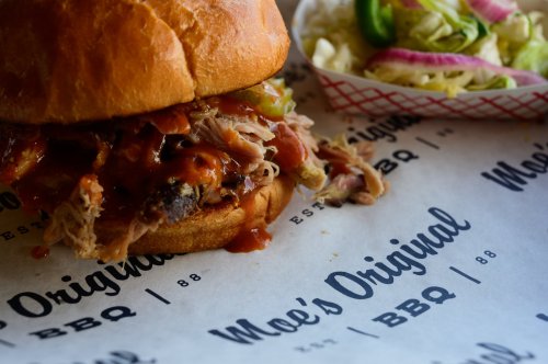 A close-up of a pulled pork sandwich with BBQ sauce, served with a side of coleslaw in a paper-lined basket.