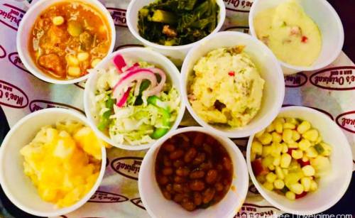 A variety of colorful side dishes in small bowls, including beans, corn, greens, and salads, arranged on a tray.