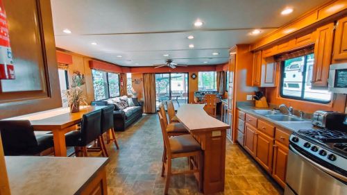 A spacious, modern kitchen and living area with wooden cabinets, a dining table, and large windows for natural light.
