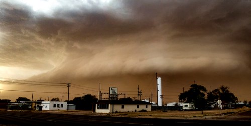 A dramatic sky with dark, swirling clouds looms over a small town, hinting at an approaching storm.
