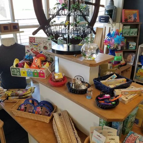 A colorful display of various crafts, toys, and gifts arranged on wooden tables in a bright store.